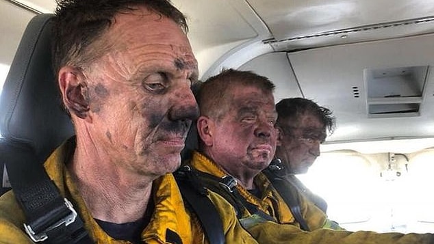 Three Tasmanian firefighters sit, exhausted and ash streaked in a vehicle