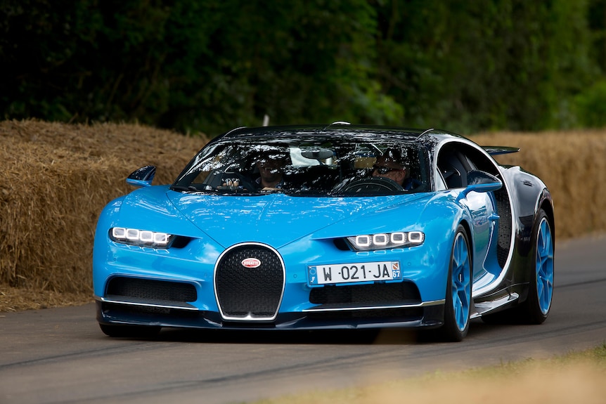A blue Bugatti Chiron is driven in country lanes with hay bales next to it