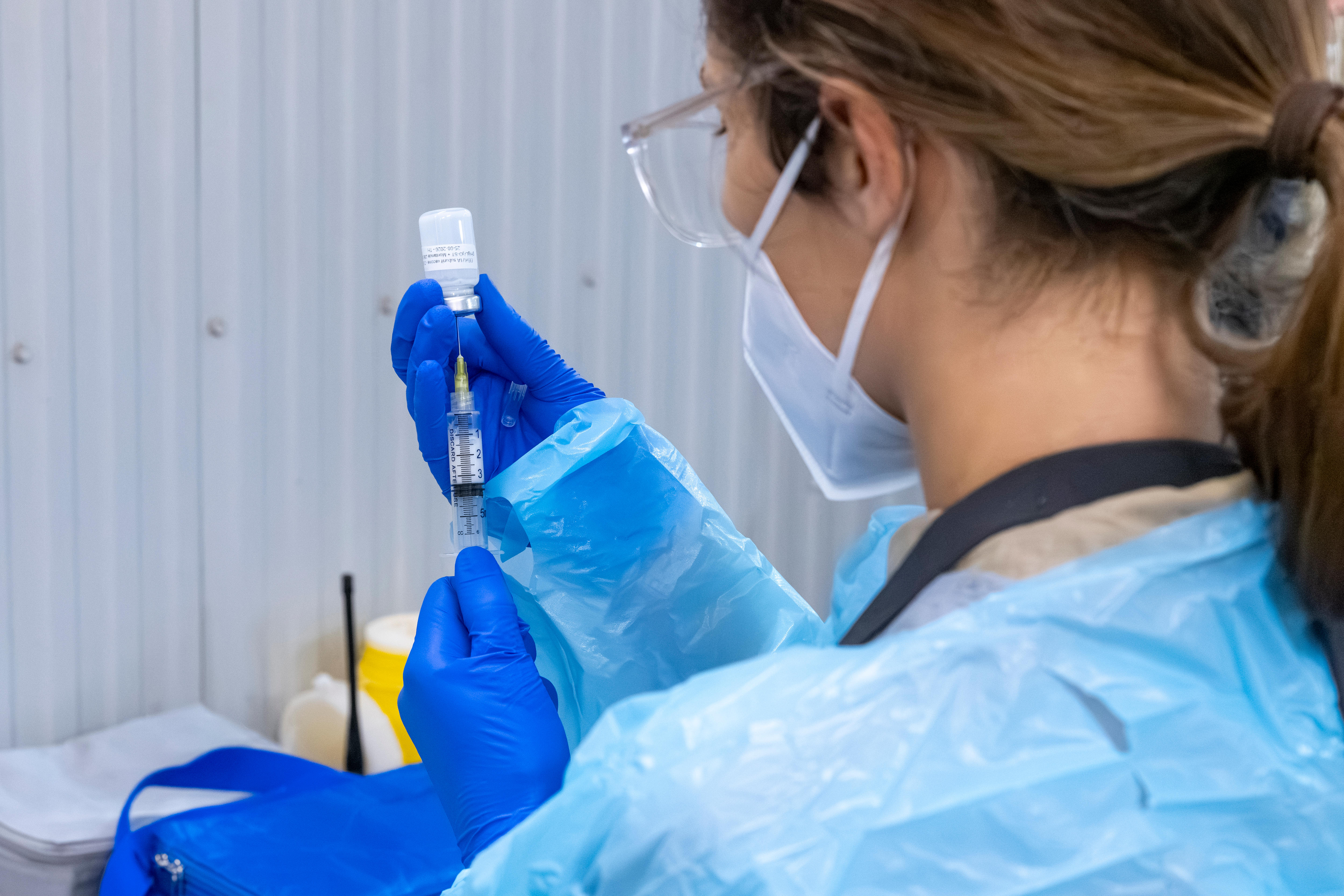 A woman wearing PPE drawing liquid into a syringe. 