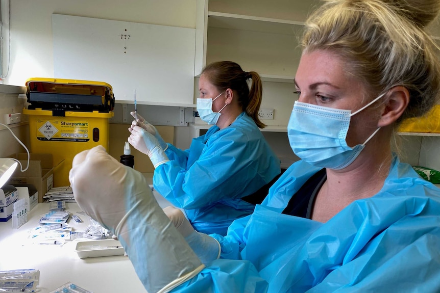 Two healthcare workers masked and in PPE check vaccinations in needles.