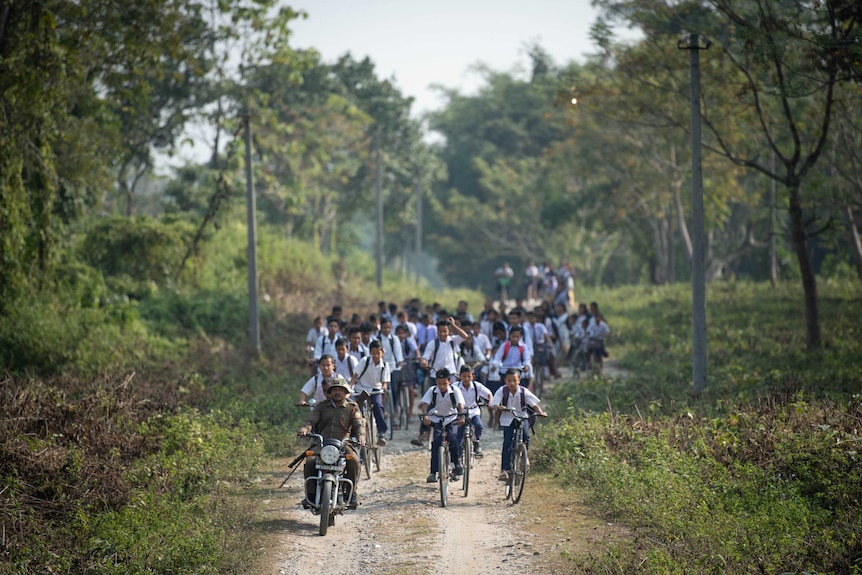Kids on bicycles follow a man on a motorbike.