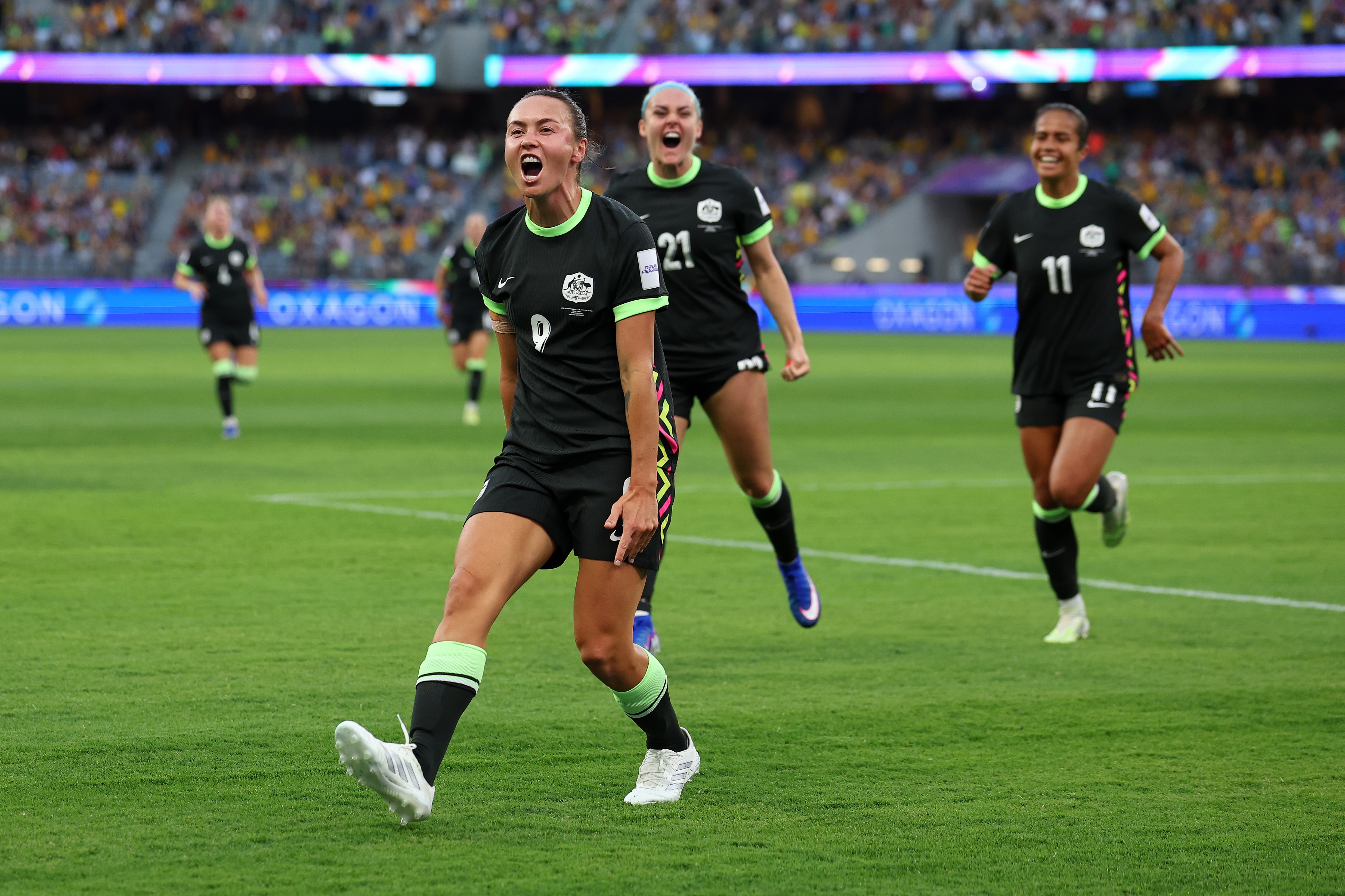 Three soccer players in dark green celebrate a goal with players in red behind them