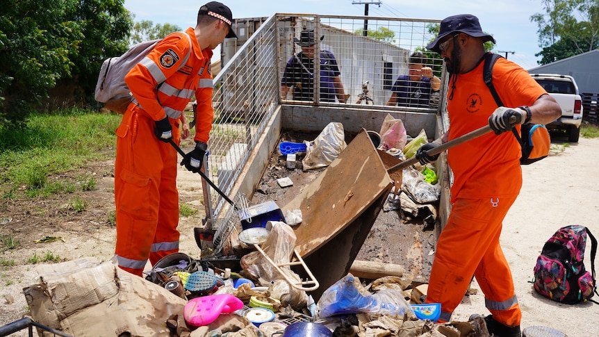 Two men in orange emergency services uniforms sweep up rubbish