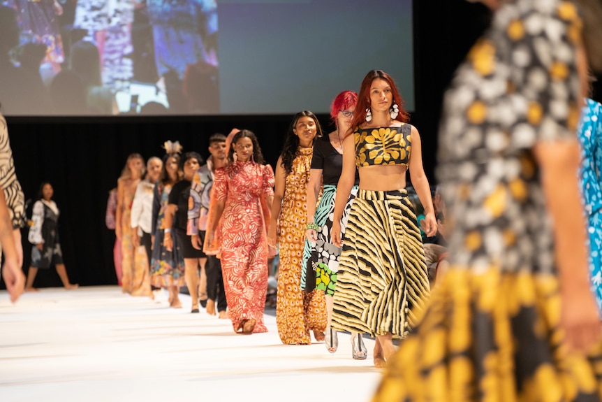 A line of First Nations models walk along the runway in bright patterned garments
