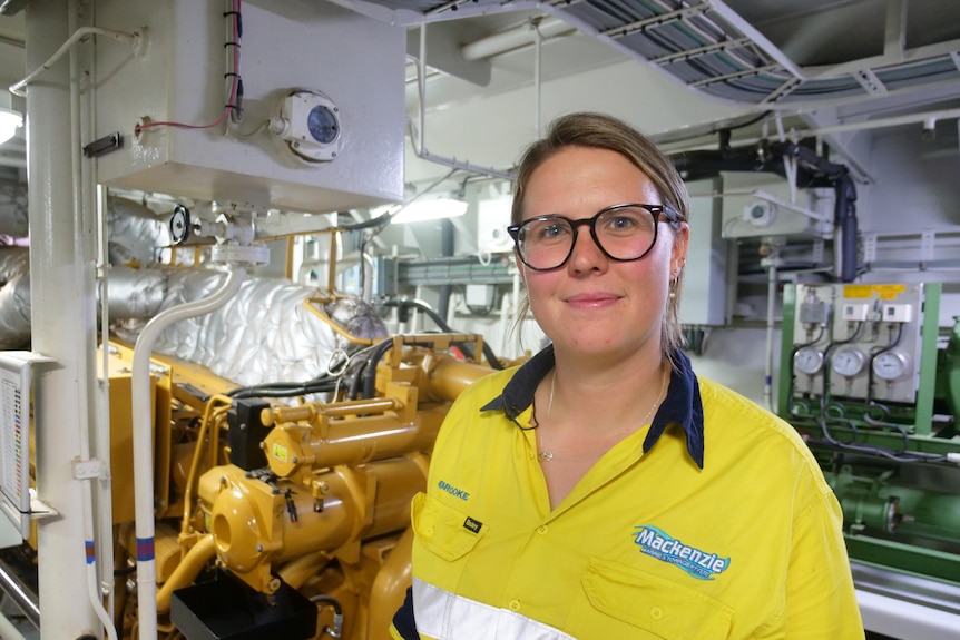 A woman wearing black glasses standing in front of a engine 