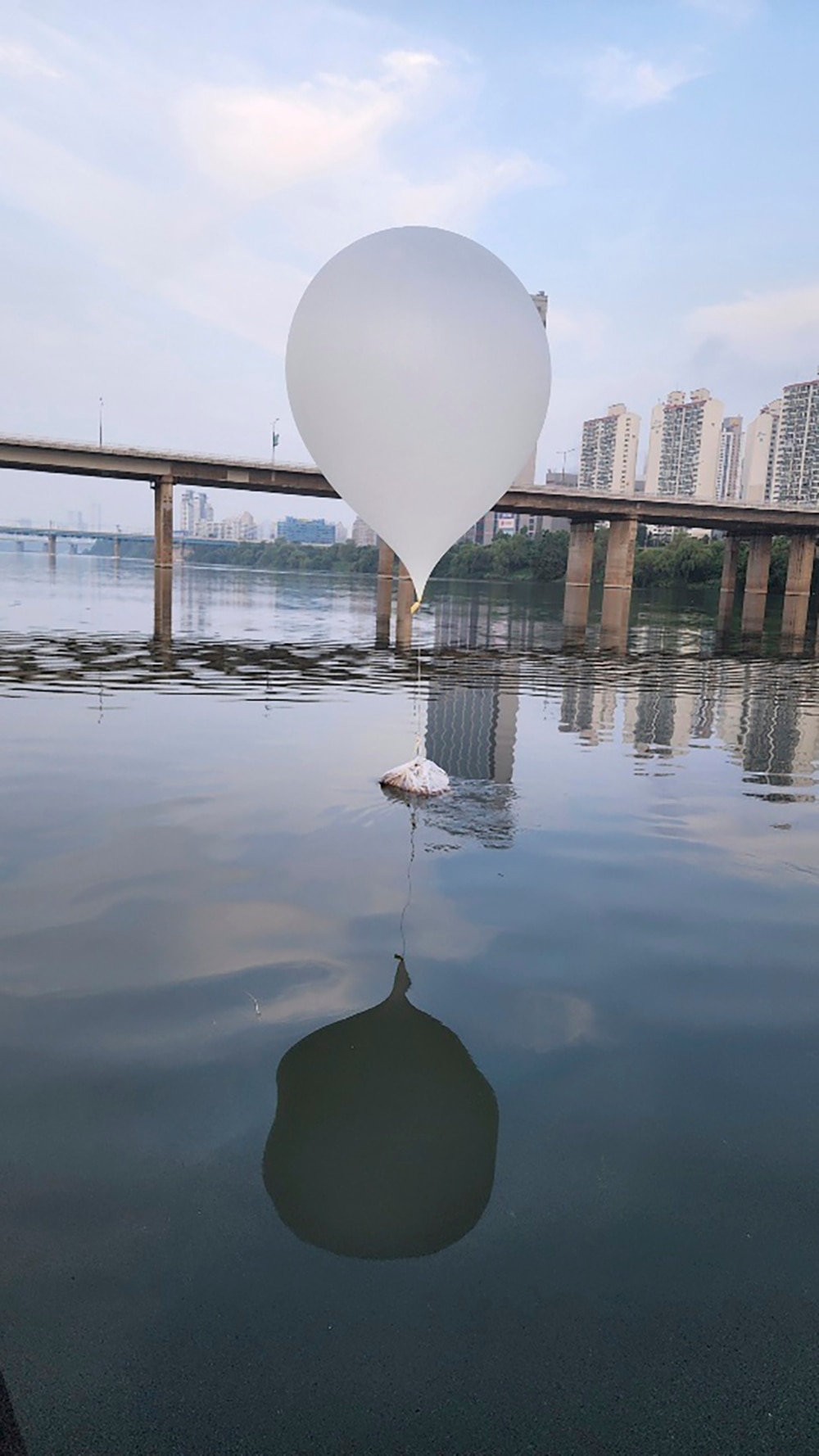 A white balloon attached via to a white bag of trash sits on a river.