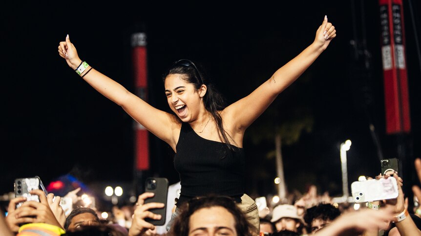 A woman elevated above a crowd of people looking excited with hands in the air