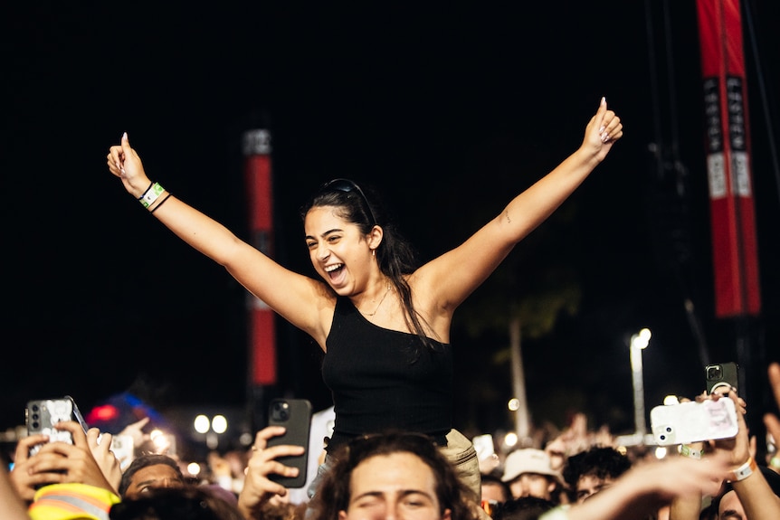 A woman elevated above a crowd of people looking excited with hands in the air
