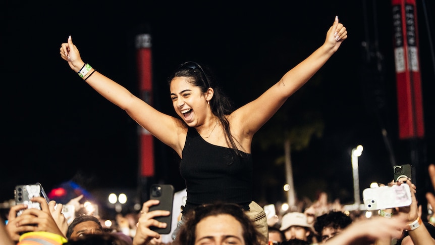 A woman elevated above a crowd of people looking excited with hands in the air