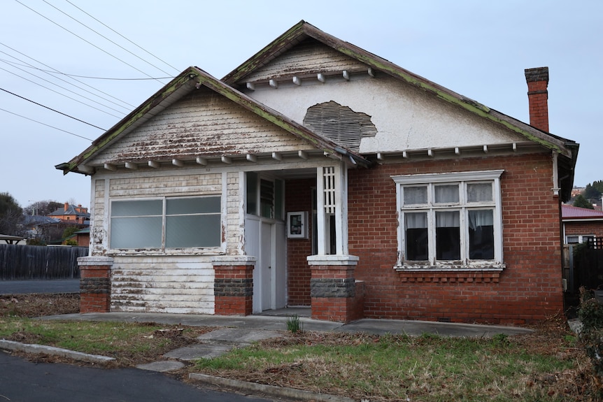 A red brick and weatherboard house with peeling paint and crumbling facade.