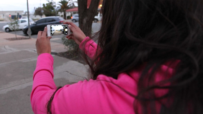 An Aboriginal woman films cars with a smartphone