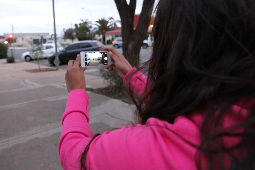 An Aboriginal woman films cars with a smartphone