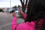 An Aboriginal woman films cars with a smartphone