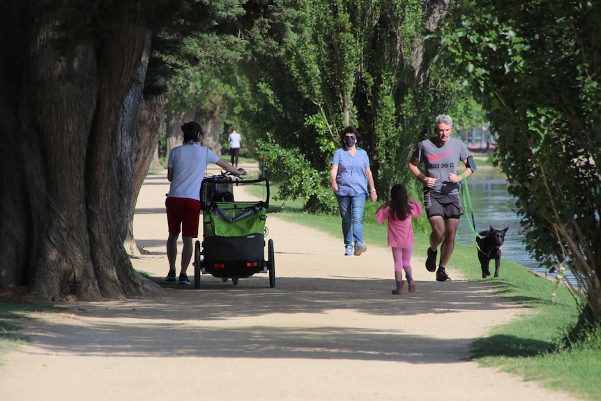 People walking in a suburban park on a sunny day next to water.