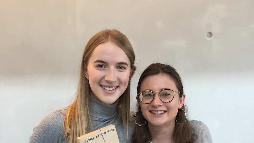 The two founders of The Unknown Project holding books wrapped in paper.