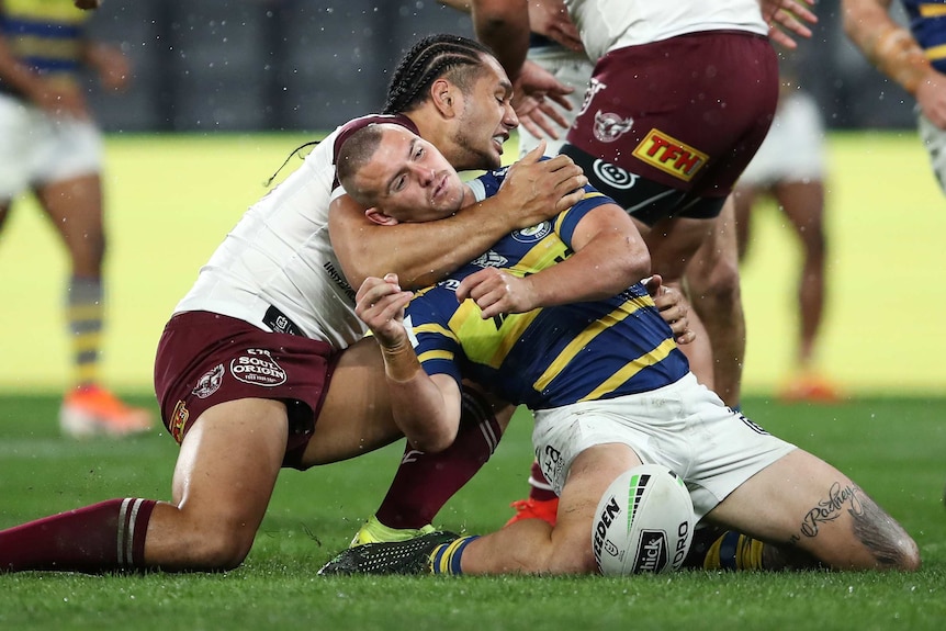 An NRL's player arm is wrapped around his opponent's neck in a high tackle.