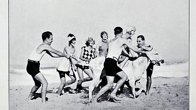 A black-and-white screenshot of a film scene where people in bathers in the 1920s are on the beach.