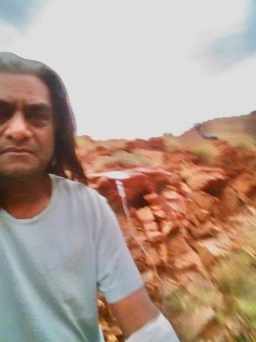 blurry photo of man with dark complexion and hair with drip in his arm standing in front of rocky mountain