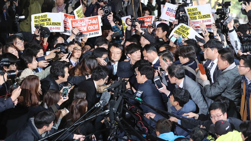 Choi Soon-sil surrounded by officers, media and protesters holding signs calling for her arrest in Seoul.