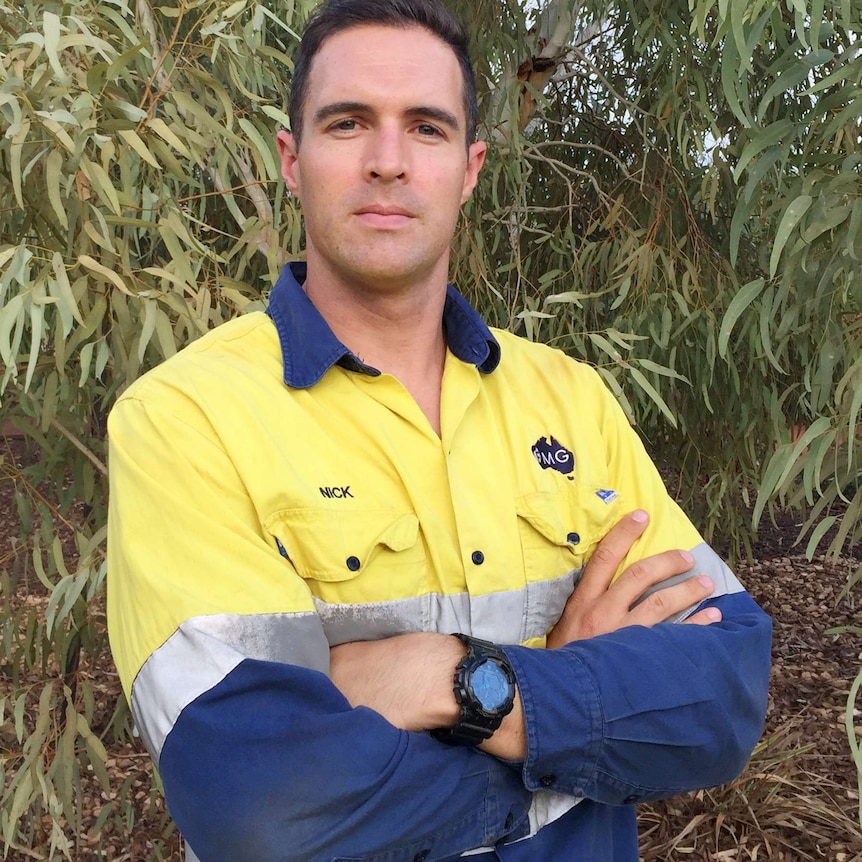 Nicholas Power poses for a photo with his arms crossed in hi-vis workwear in front of trees.