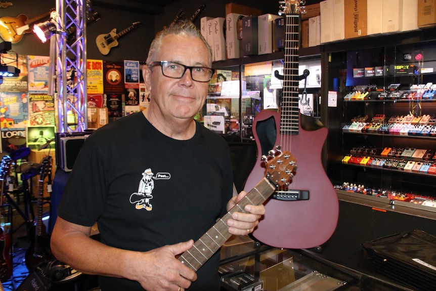 A man standing in a music shop holds the neck of a guitar.
