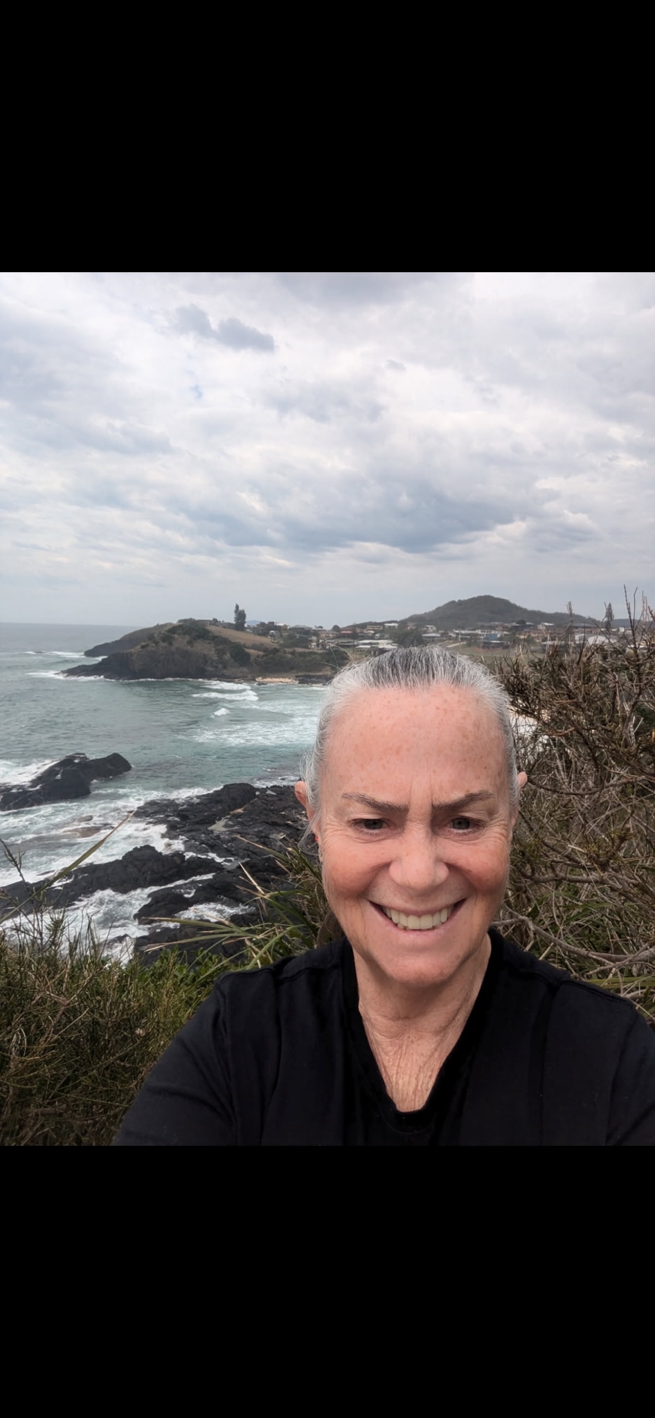     Jann Alhafny se hace un selfie con el pelo gris recogido, de pie sobre un acantilado costero.