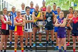 All the AFLW team captains, in their full kits, stand on steps around the premiership cup.