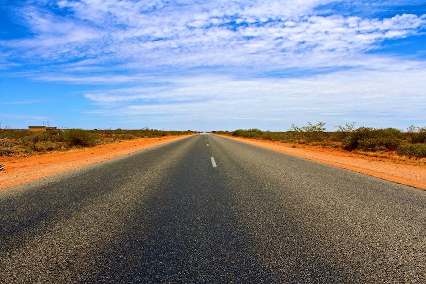 The North West Highway stretches on towards the horizon near Carnarvon, with red dirt and scrub on either side.