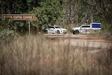 Two police vehicles parked close together, on a small road surrounded by bush. A sign nearby reads 'Cutta Cutta Caves'.