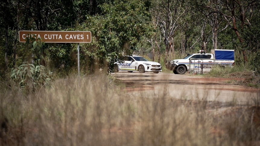 Two police vehicles parked close together, on a small road surrounded by bush. A sign nearby reads 'Cutta Cutta Caves'.