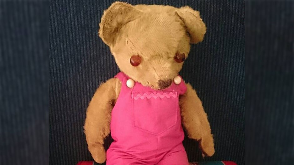 A teddy bear with leather button eyes and pink overalls