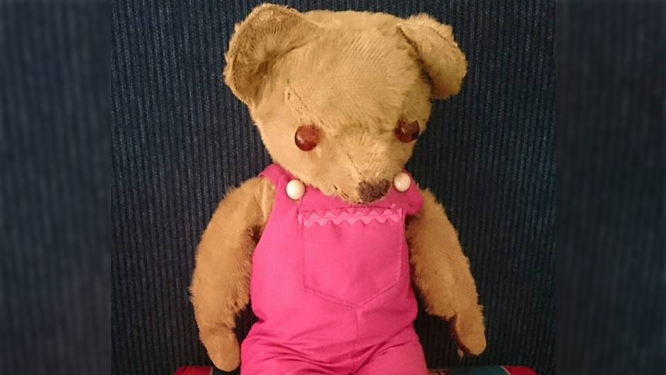 A teddy bear with leather button eyes and pink overalls