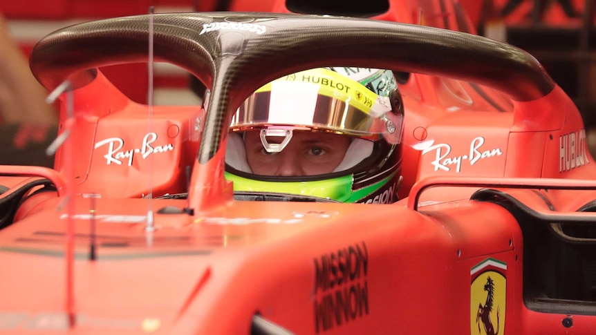 An F1 driver sits in the cockpit of his Ferrari with only part of his face visible through his helmet.