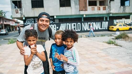Native Guna man in his late twenties leans down and hugs three young kids in El Chorrillo