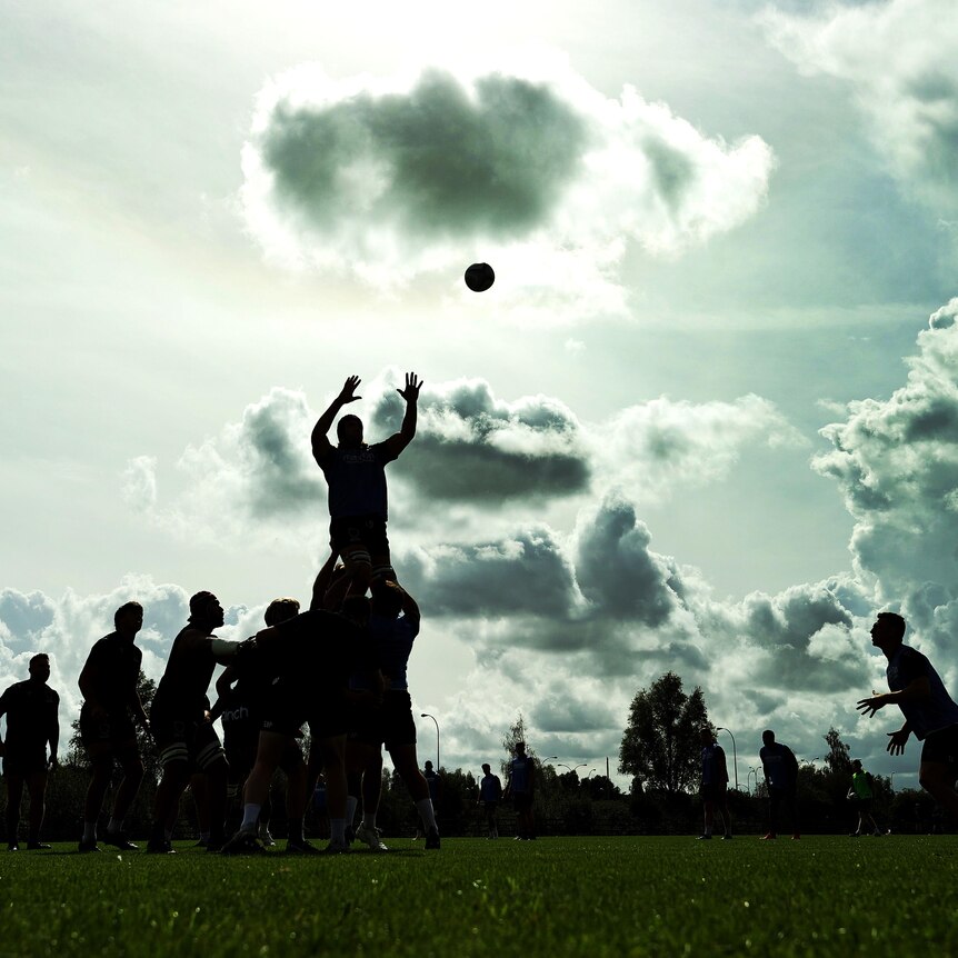 A photo of silhouetted rugby players in training with one man being lifted in a lineout to take the ball as others watch.