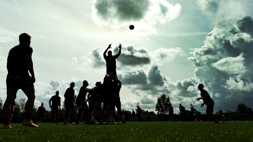 A photo of silhouetted rugby players in training with one man being lifted in a lineout to take the ball as others watch.
