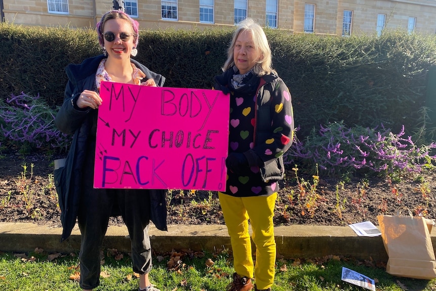 Two women with a pink sign standing on a lawn.