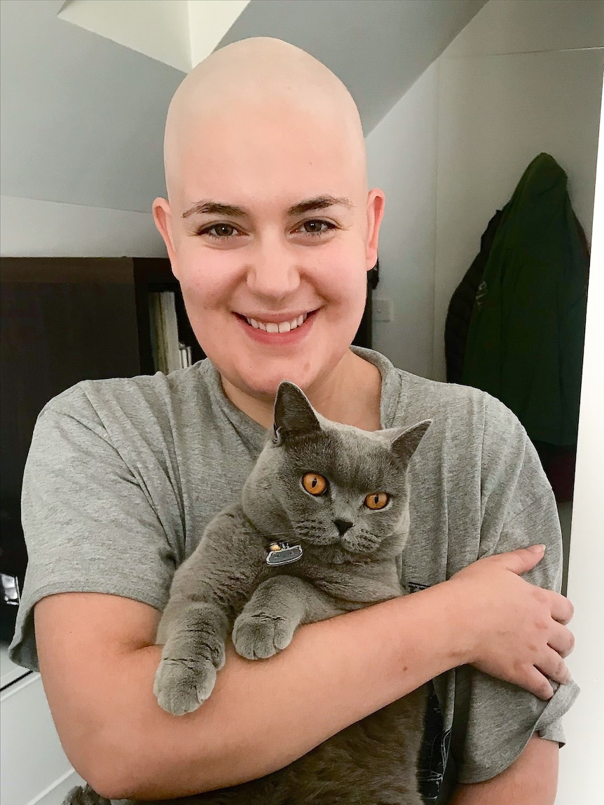 A woman without hair smiling at the camera while holding a cat.