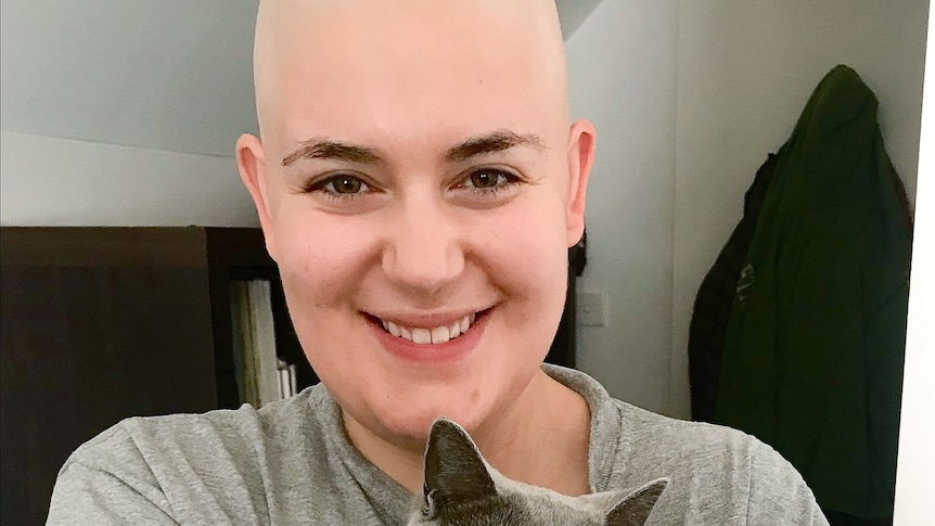 A woman without hair smiling at the camera while holding a cat.