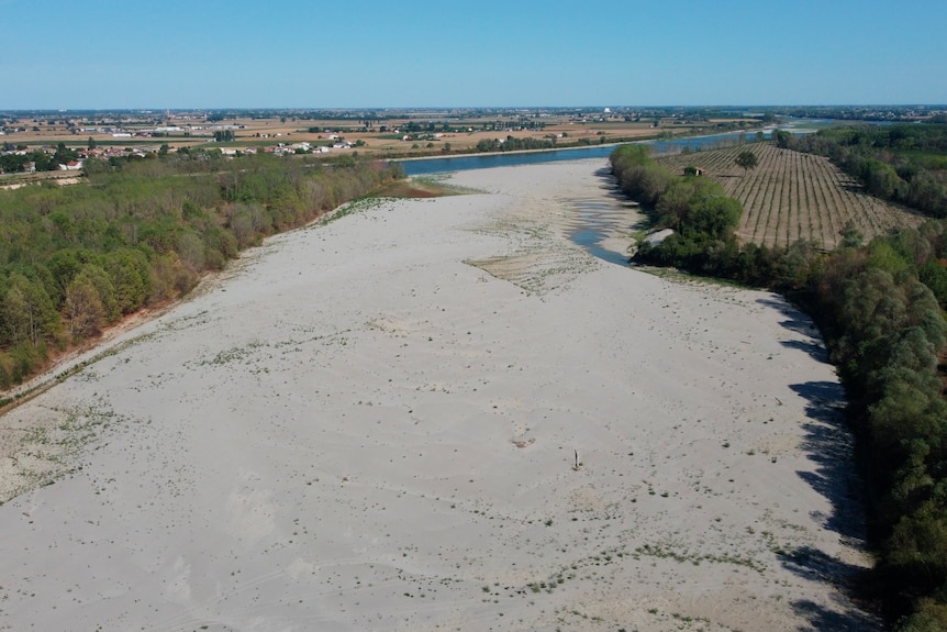 A dry river bed runs to a low river that travels into the distance past fields and a village.
