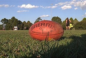 A red Sherrin AFL football lies on grass.