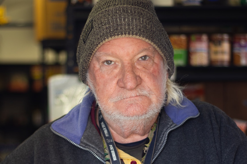 A man in a beanie stands at a small window looking out