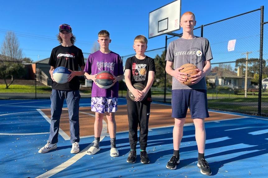 four teens stand in a row holding basketballs 