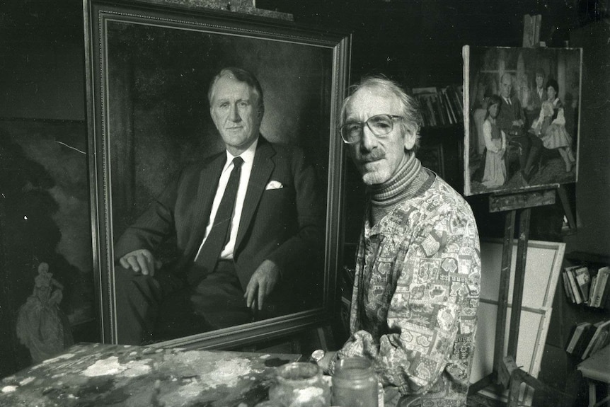 A black and white photo of painter Paul Fitzgerald standing next to a painting of Malcolm Fraser.