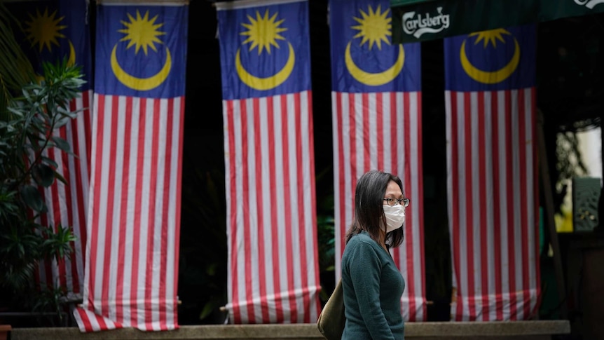 A woman wearing a face mask crosses a street with national flags on display to celebrate Malaysia Day.
