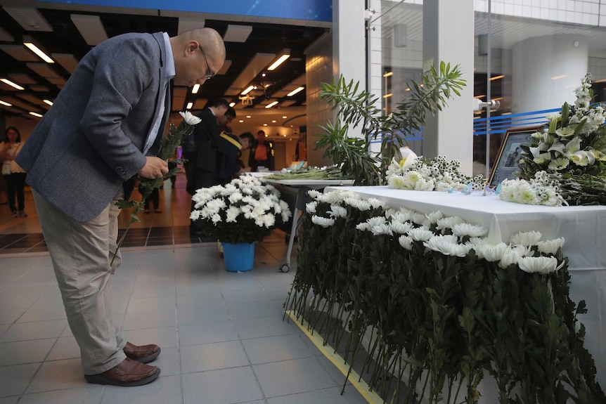 A man bows to a table with a photo of the victim and flowers on it