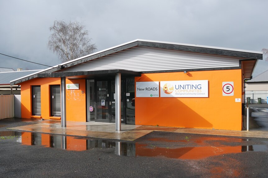 An orange building with grey roof, Uniting Communities, New Roads, sign on the front.