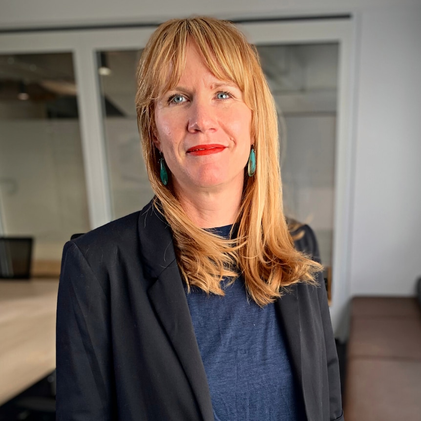 Woman with reddish-blonde hair wearing a black suit. 