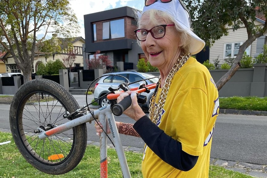 An older woman pretending to do a wheelie on a push bike.