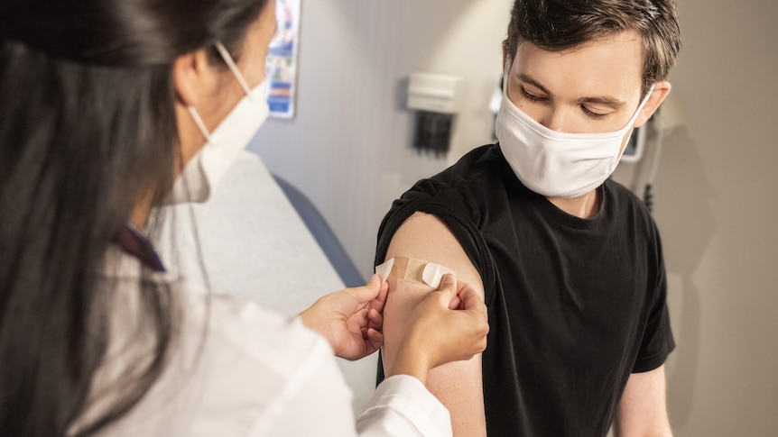 A man looks at his upper arm where a woman is putting on a bandaid. 